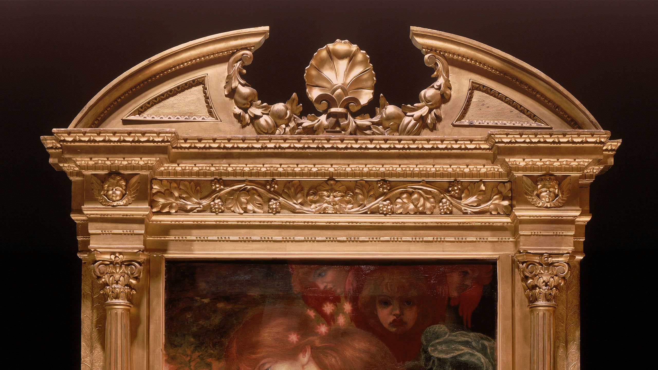 Elaborate gold frame decorated with vines and a cherub's head on the pedestal at each side